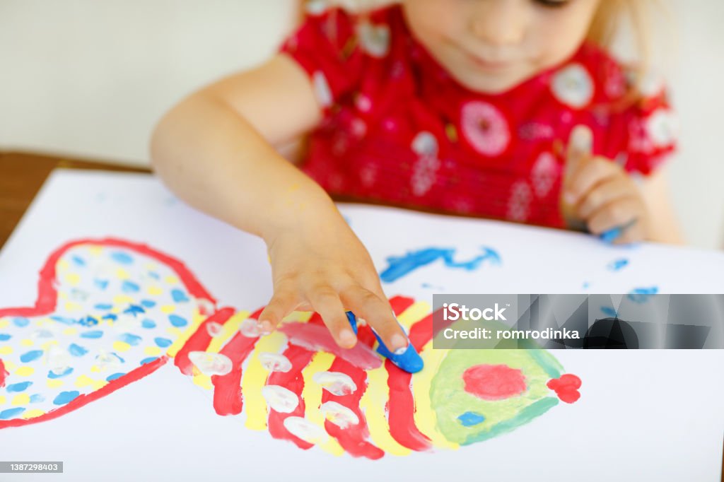 Little creative toddler girl painting with finger colors a fish. Active child having fun with drawing at home, in kindergaten or preschool. Education and distance learning for kids. Creaitve activity. Little creative toddler girl painting with finger colors a fish. Active child having fun with drawing at home, in kindergaten or preschool. Education and distance learning for kids. Creaitve activity Toddler Stock Photo