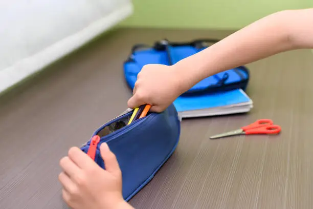 Photo of A child's hands holding some paints in a blue case for school. On a table is a backpack and scissors. Back to school concept