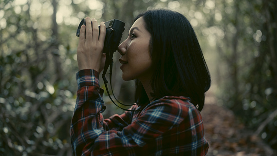 Asian woman travels and uses a camera to capture memories in a tropical forest.