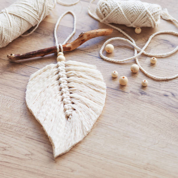 istock Macrame leaf  in natural color and thread windings lying on a wooden table. Cotton rope decor macrame to make your room more cozy and unique. Woman hobby. Handmade wall hanging decor. Copy space 1387305955