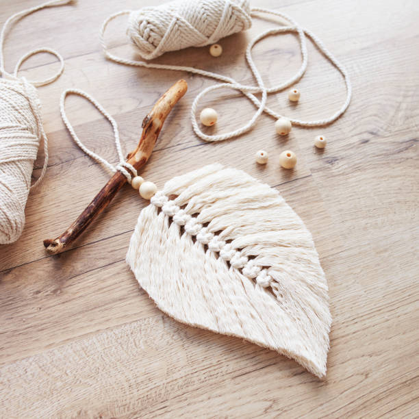 istock Macrame leaf  in natural color and thread windings lying on a wooden table. Cotton rope decor macrame to make your room more cozy and unique. Woman hobby. Handmade wall hanging decor. Copy space 1387305959