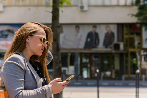 Woman sitting and using a smart phone at the street in a sunny summer day