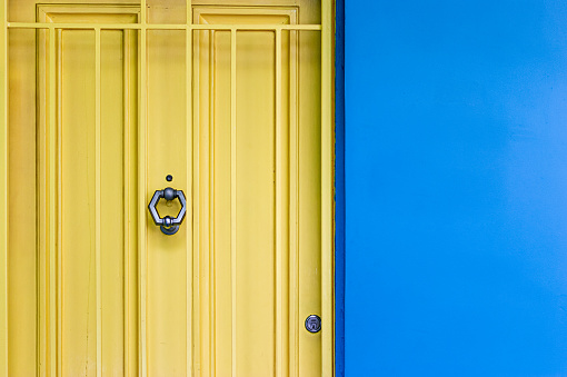 Detail image of a home exterior with a bright yellow door and security gate with metal door knocker and vibrant plain blue wall