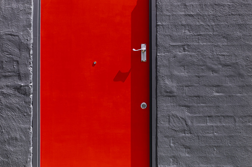 Close up detail of a building exterior with a bright red door contrasting against a dark grey brick wall