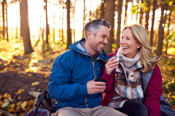 coppia di pensionati maturi che si fermano per riposare e bere caldo a piedi attraverso la campagna autunnale o invernale - couple foto e immagini stock