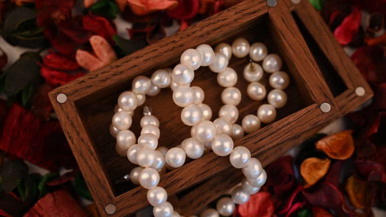 Naszyjniki z pereł w drewnianym pudełku otoczonym kolorowymi suszonymi płatkami to biżuteria inspirowana sztuką.