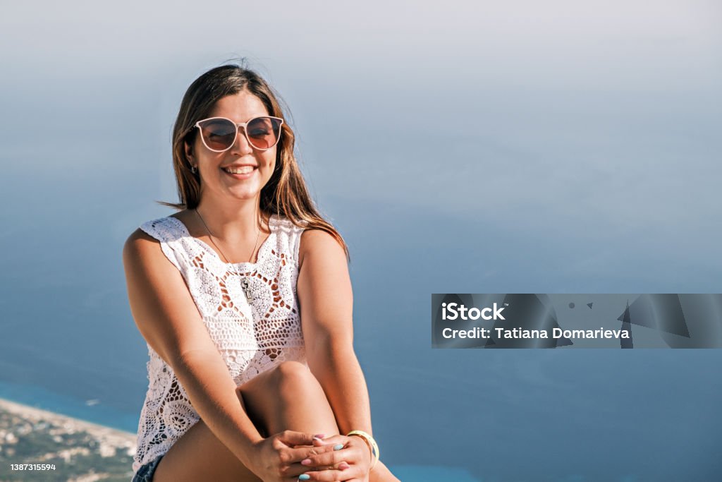 happy smiling brunette girl on sitting in the background of the sea in sunglasses happy smiling brunette girl sitting on the background of the sea in sunglasses Albania Stock Photo