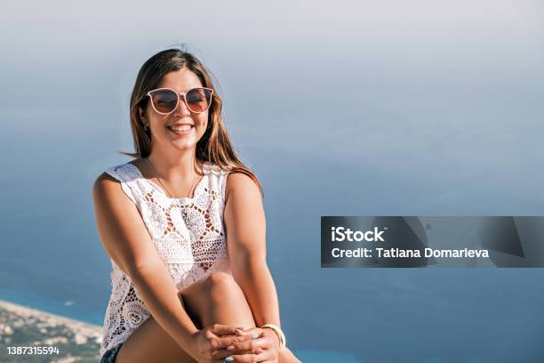 Happy Smiling Brunette Girl On Sitting In The Background Of The Sea In Sunglasses Stock Photo - Download Image Now