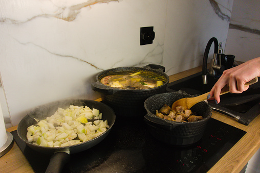 Woman preparing Sunday dinner on electric induction hob. Broth and meat with sauce is preparing