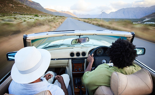 Rear view of a mature African couple driving in a convertible along a scenic road in the late afternoon