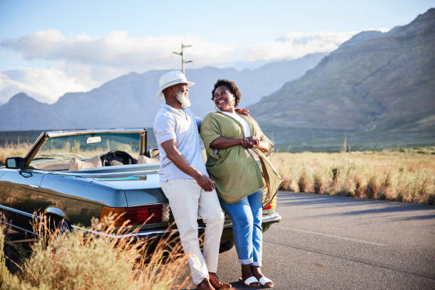 istock Mature couple laughing while leaning against their car during a road trip 1387321177