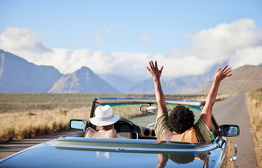 Rear view of an African woman sitting with her arms raised in the air during a scenic road trip in a convertible with her husband