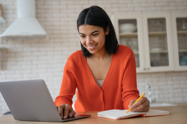 African American student studying, online education concept. Portrait of beautiful confident businesswoman using laptop computer taking notes working from home. Successful business stock photo