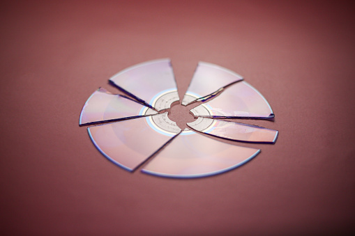 Broken compact disc divided into parts close-up on a red-burgundy background, complete loss of data