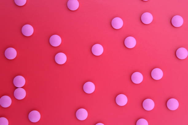 istock Many pink pills are scattered on a red background. 1387325260