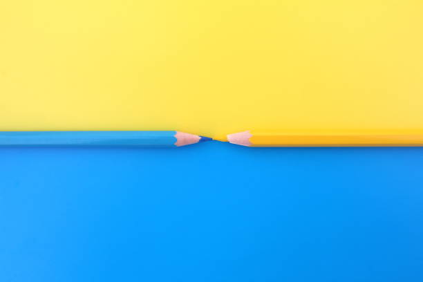 istock Yellow and blue pencils lie simultaneously on the same colors background with space for text. 1387325613