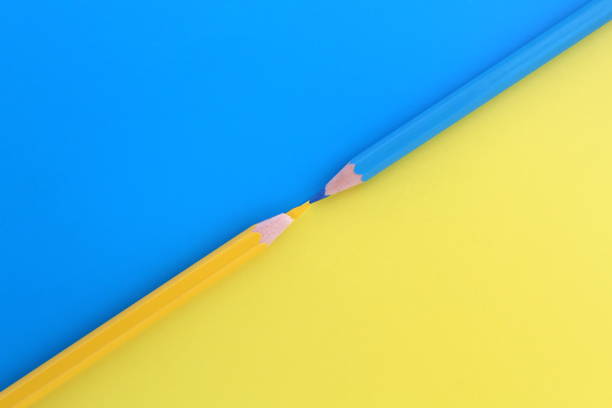 istock Yellow and blue pencils lie simultaneously on the same colors background with space for text. 1387326170