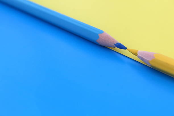 istock Yellow and blue pencils lie simultaneously on the same colors background with space for text. 1387326213