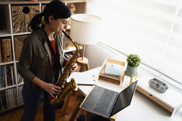 istock Female musician standing and playing saxophone while watching online tutorial on laptop 1387326517