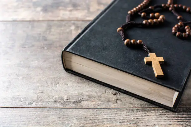 Rosary catholic cross on Holy Bible on wooden table