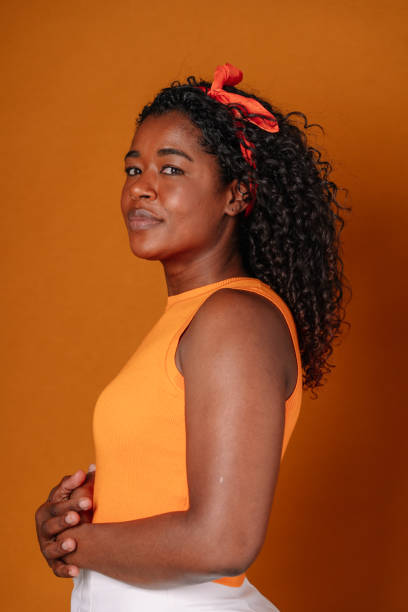 mid-waist-porträt einer afroamerikanischen frau mit dunklen haaren und orangefarbener kleidung. - afro amerikanischer herkunft stock-fotos und bilder