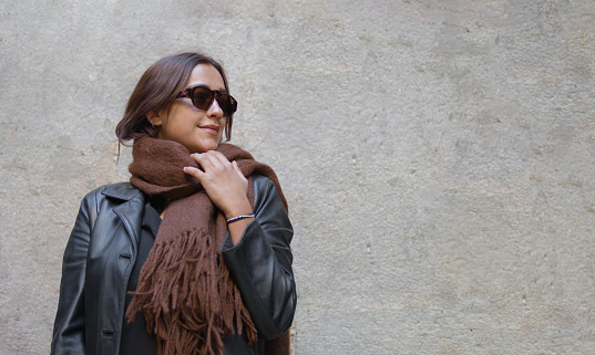 portrait headshot of a pretty woman with hispanic features wearing sunglasses and a brown scarf while is standing ahead a unicolor background