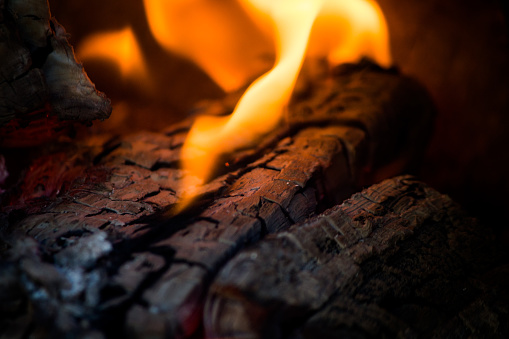 A close up of orange flames omitting from a charred wooden surface.