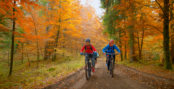 Young man and woman riding mountain bikes on dirt track passing through autumn forest.