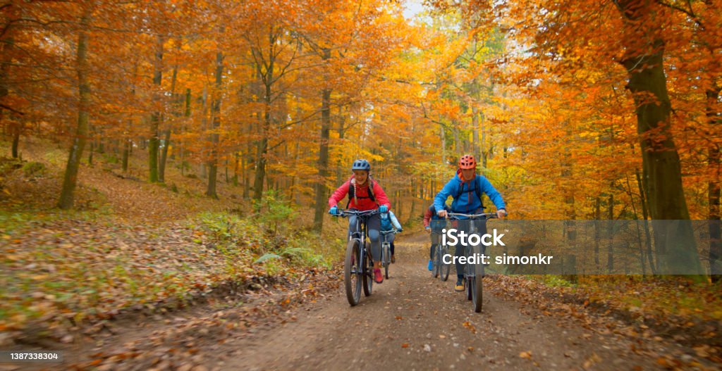 Young friends mountain biking in autumn forest Young man and woman riding mountain bikes on dirt track passing through autumn forest. Autumn Stock Photo