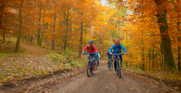 Young friends mountain biking in autumn forest Young man and woman riding mountain bikes on dirt track passing through autumn forest. red white blue bike stock pictures, royalty-free photos & images
