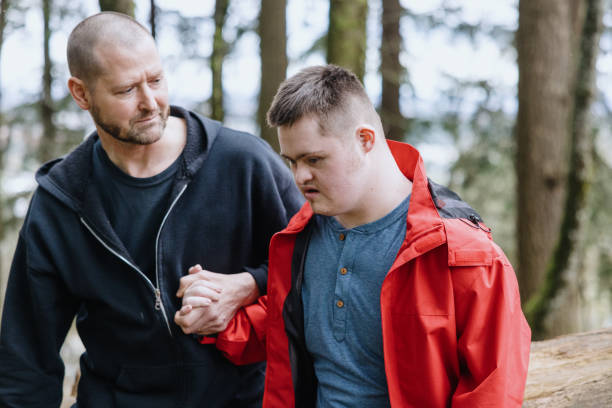 Caretaker Hiking With Adult Disabled Man Two Caucasian men hike on a woodland trail in the Pacific Northwest, the father of an adult man with Down Syndrome holding his sons hand. disabled person hiking outdoors stock pictures, royalty-free photos & images