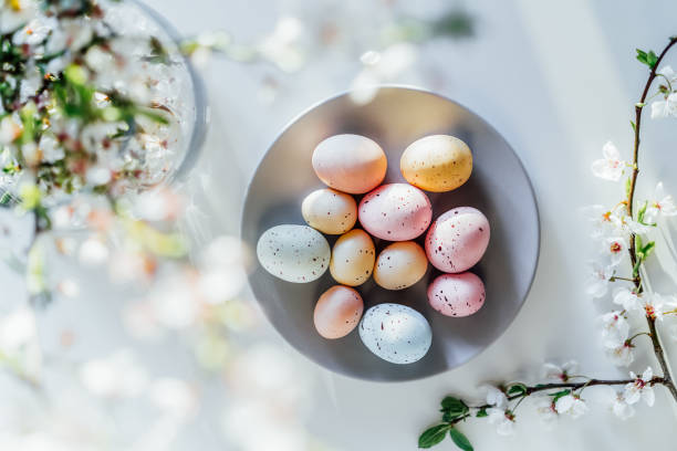 istock Top view colored easter eggs on the gray plate, blooming tree branch in vase and flower petals on the white table. Happy Easter and springtime card. Minimalism and simplicity. Selective focus. 1387339992