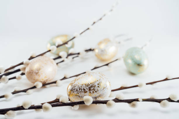 istock Blooming pussy willow branches and golden eggs in different patterns and colors on the white background. Minimalist, Modern Happy easter card. Selective focus, copy space. 1387340006