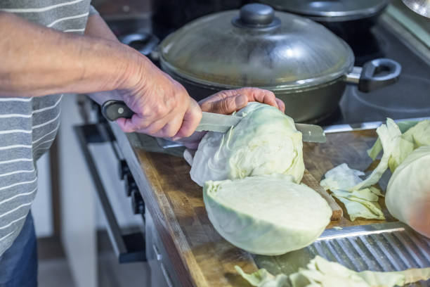 Old woman granny cutting a white cabbage in the kitchen with knife and wooden board next to the sink and stove on the work surface, Germany Old woman granny cutting a white cabbage in the kitchen with knife and wooden board next to the sink and stove on the work surface, Germany white cabbage stock pictures, royalty-free photos & images