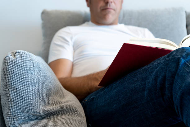 istock Unrecognizable man in an armchair reading a book. Focus on the book 1387341381