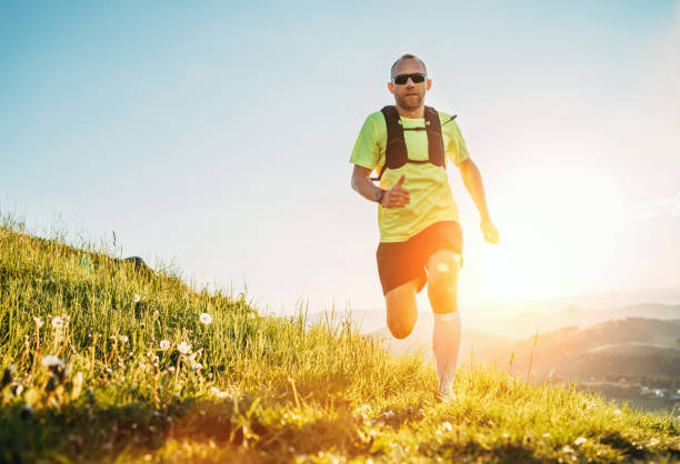 Active mountain trail runner dressed bright t-shirt with backpack in sport sunglasses running endurance marathon race by picturesque hills at sunset time. Sporty active people concept image. stock photo