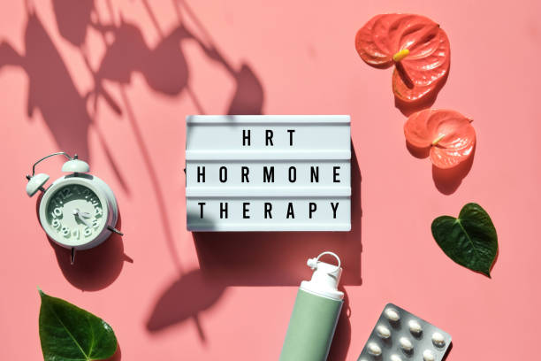 Text HRT Replacement Therapy on light box. Menopause, hormone therapy concept. Pink background with alarm clock, exotic leaves, pills, estrogene gel stock photo