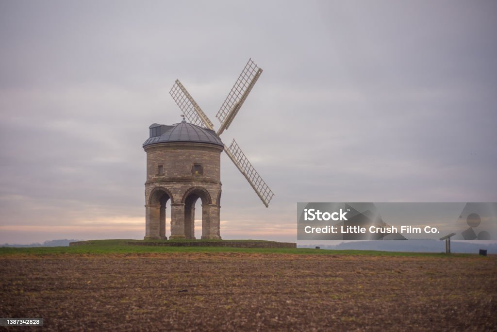 Rural windmill at sunset A traditional windmill stands in a rural field at sunset. Agricultural Activity Stock Photo