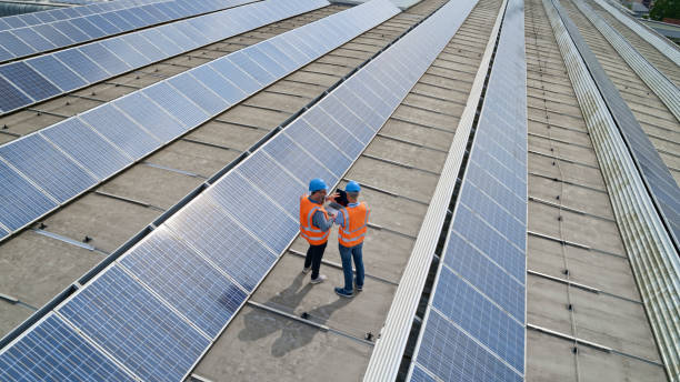 Engineers using laptop on rooftop Mature men engineer working on laptop while standing on the rooftop of solar power plant. two men same clothes stock pictures, royalty-free photos & images