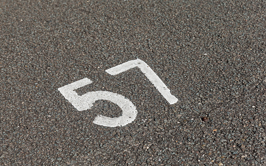 Daytime close-up of the number 57 painted in white on the asphalt of a parking lot