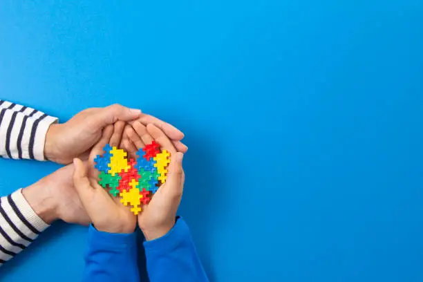World autism awareness day concept. Adult and kid hands holding puzzle heart on light blue background