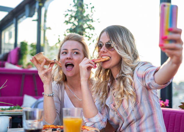 istock women take pictures and eat pizza 1387351752