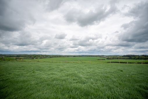 Clouds gather above grass farmland stretching towards the horizon.