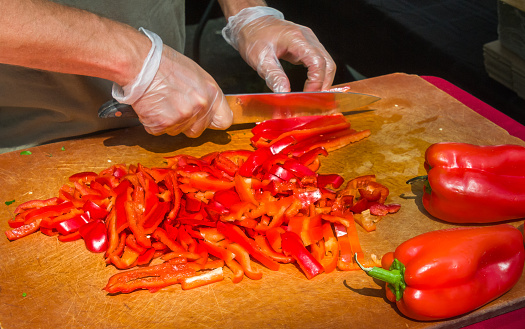 A chef slices red peppers on a wooden cutting board in preparation  of adding them to a pizza at an outdoor farmers market on Cape Cod.