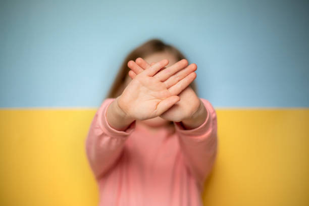 Child gesturing stop with both hands, Ukrainian flag in background