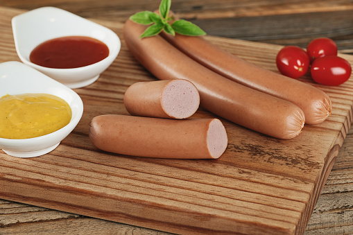 Sausage, cherry tomatoes, basil, ketchup and mustard sauce on wooden chopin board. Horizontal photo.