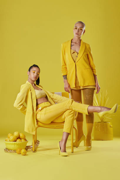 Shot of two women dressed in stylish yellow clothes against a yellow background How lovely yellow is haute couture stock pictures, royalty-free photos & images