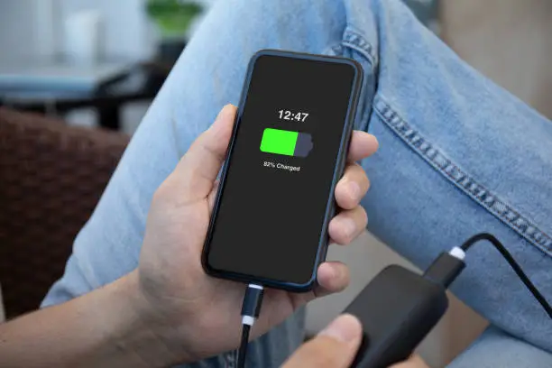 Man hands holding phone with charged battery on the screen connected to powerbank charge