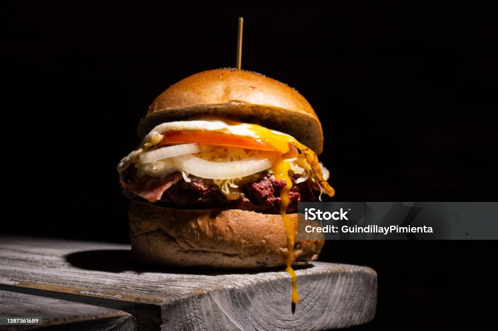 Home made tasty burger on wooden table and black background Home made tasty burger with melting cheese on wooden table and black background Backgrounds Stock Photo