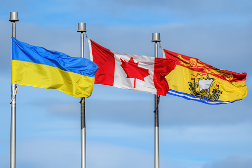 Ukrainian, Canadian, and New Brunswick flags fly in a row. Many Canadians are flying Ukraine flags in support of Ukraine during the Russian invasion.
